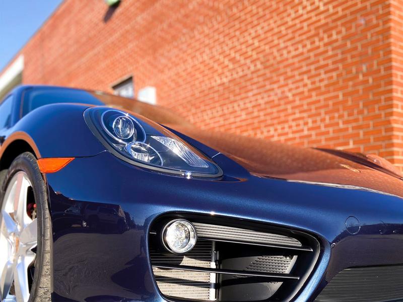 Front corner close up of a blue porsche cayman in front of brick building