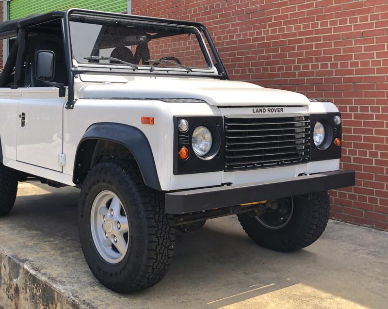 White Classic Land Rover Defender 90 with brick wall backdrop